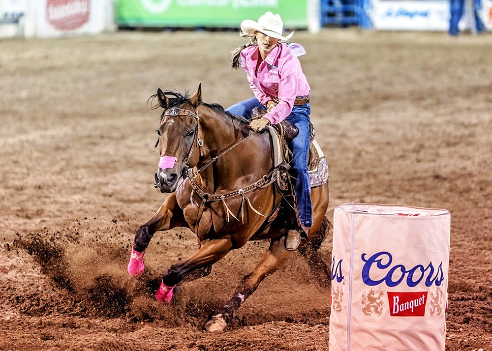 Woman riding a horse around a Coors Banquet barrel in a rodeo setting
